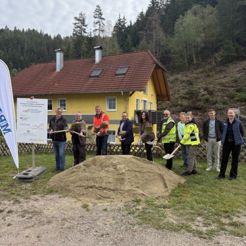 Spatenstich in Gremmelsbach mit Vertretern der Stadtverwltung, der Baufirma, des Planungsbüros und des Zweckverbands. Alle stehen vor einem großen Sandhaufen und werfen mit Spaten Sand in die Luft