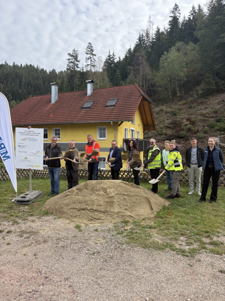 Spatenstich in Gremmelsbach mit Vertretern der Stadtverwltung, der Baufirma, des Planungsbüros und des Zweckverbands. Alle stehen vor einem großen Sandhaufen und werfen mit Spaten Sand in die Luft
